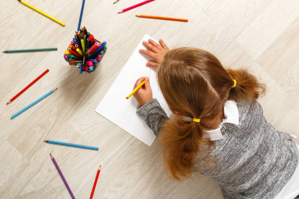vista dall'alto di una bambina sdraiata e dipinto sul pavimento nella sua stanza a casa. - left handed foto e immagini stock