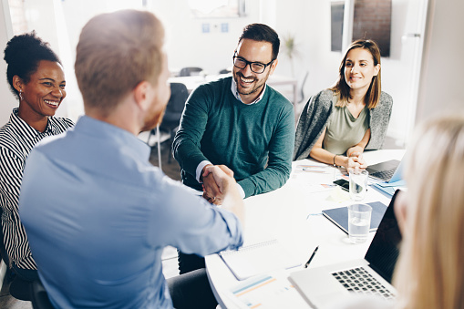 Happy businessmen shaking hands during a meeting with their female colleagues in the office.