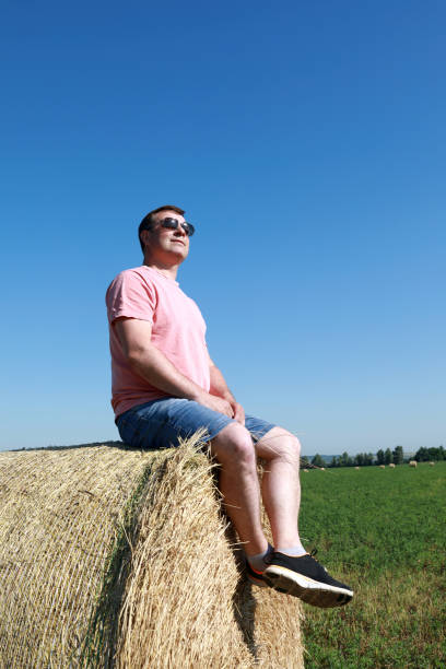 Person resting on bale of straw on field