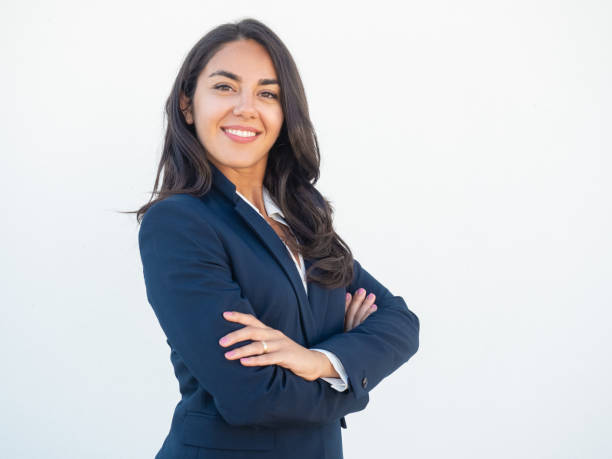 Smiling confident businesswoman posing with arms folded Smiling confident businesswoman posing with arms folded. Happy beautiful black haired young Latin woman in formal suit standing for camera over white studio background. Corporate portrait concept businesswear stock pictures, royalty-free photos & images