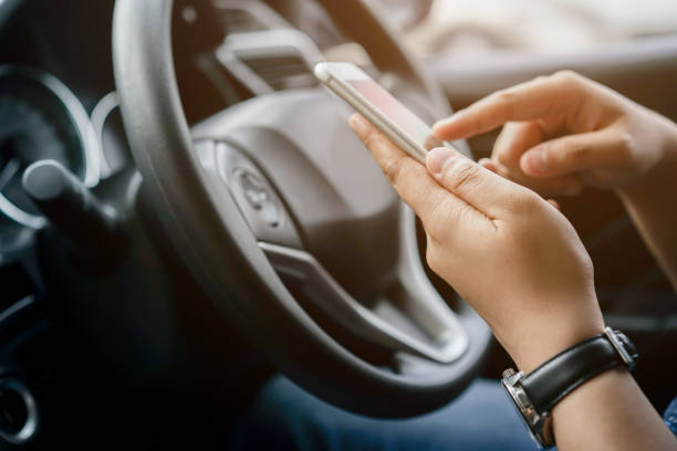 旅行先のgpsナビゲーションを使用するためのドライバーの女性手持ちスマートフォンをクローズアップし、駐車中に連絡先のためのwebブラウザやテキストメッセージオンラインでデータを読� - タクシー 写真 ストックフォトと画像