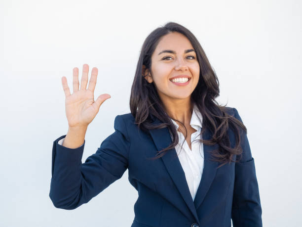 Positive friendly businesswoman making greeting gesture Positive friendly businesswoman making greeting gesture. Front view of smiling beautiful young Latin woman in office suit waving hand and saying hello. Gesturing concept waving gesture stock pictures, royalty-free photos & images