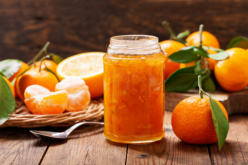 glass jar of orange tangerine or mandarin jam with fresh fruits on wooden table