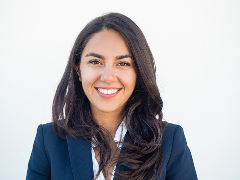 Happy successful businesswoman smiling at camera over white studio background. Closeup of beautiful black haired young Latin woman wearing formal jacket and smiling. Business portrait concept