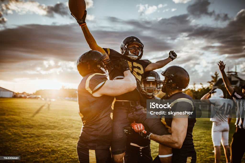 Victory on American football match! Team of American football players celebrating victory at sunset. American Football - Sport Stock Photo