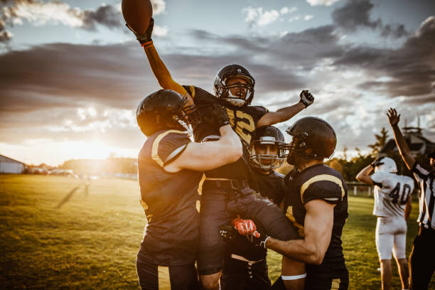 Victory on American football match! Team of American football players celebrating victory at sunset. football team stock pictures, royalty-free photos & images