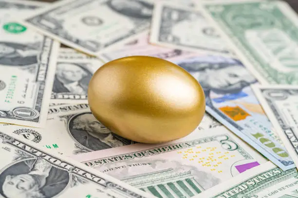 Photo of Shiny golden egg on pile of US America dollar banknotes money metaphor of finding the unbelievable good stock with high dividend or success investment in stock market concept