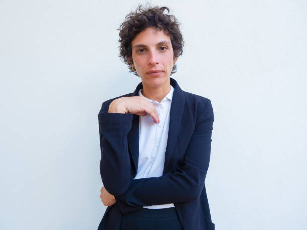 Portrait of serious confident androgynous businesswoman Portrait of serious confident androgynous businesswoman. Young woman in office suit standing for camera with folded arms over studio background. Female business leader concept lgbtqcollection stock pictures, royalty-free photos & images
