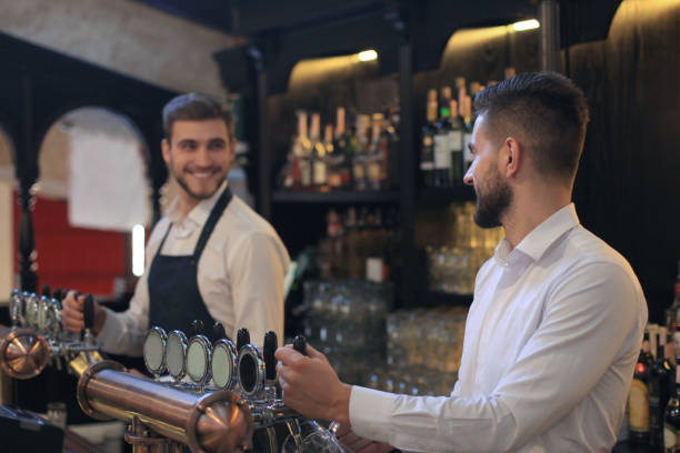istock Handsome bartender is smiling and filling a glass with beer while standing at bar counter in pub. 1163323408