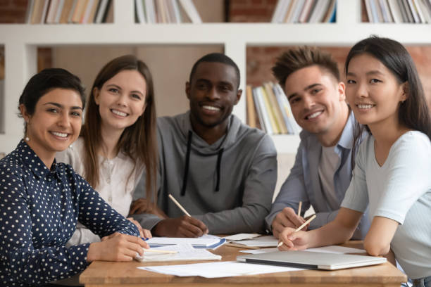 Smiling multiracial groupmates smiling posing for picture Group picture of happy multiethnic young people sit at shared desk look at camera studying together, multicultural excited students or groupmates smiling posing for photo working in library multi ethnic group college student group of people global communications stock pictures, royalty-free photos & images