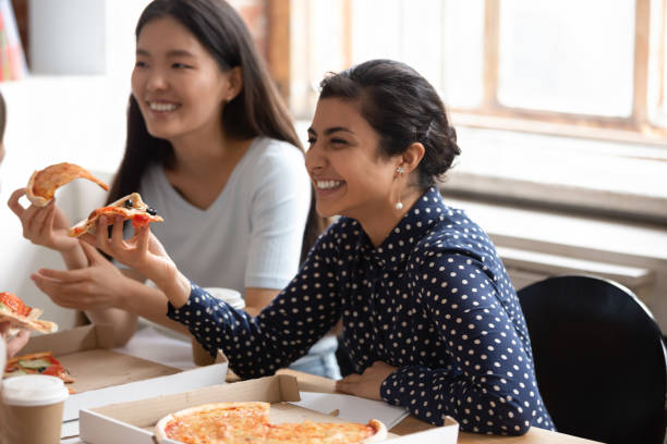 istock Smiling diverse groupmates have fun eating pizza in office 1163323475