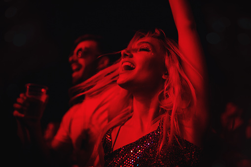 Young couple dancing at music festival. They are jumping with their arms raised illuminated with red stage light.