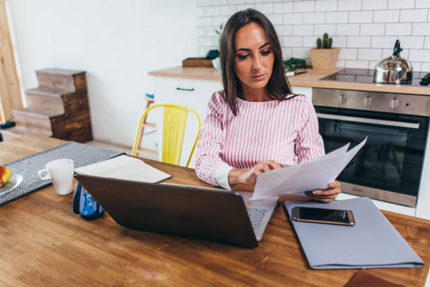 istock Woman working with documents and laptop in the kitchen at home 1163328495