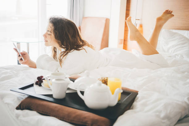 Woman having breakfast Woman having breakfast in the hotel room. Tray with breakfast on a bed. Girl looking at the phone and smile. bed breakfast pictures stock pictures, royalty-free photos & images