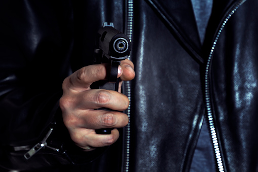 Male hand holding a gun on the background of a leather jacket. Close-up