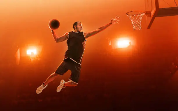 African american professional basketball player with a ball on floodlight professional court scoring a goal