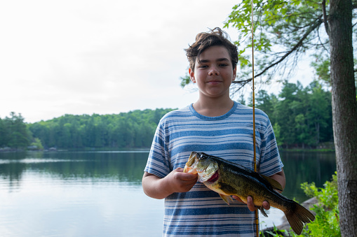 The boy shows Fishy's catch hanging on his hook. Sport fishing on the river in summer.