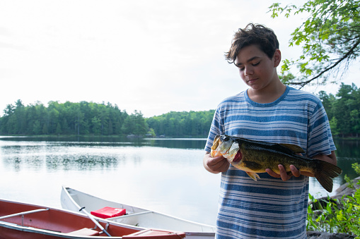 A proud teen fisherman with a nice Largemouth bass he has caught (real)