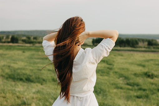 Close up portrait of beautiful carefree long hair girl in the white clothes in field, view from back. Sensitivity to nature concept