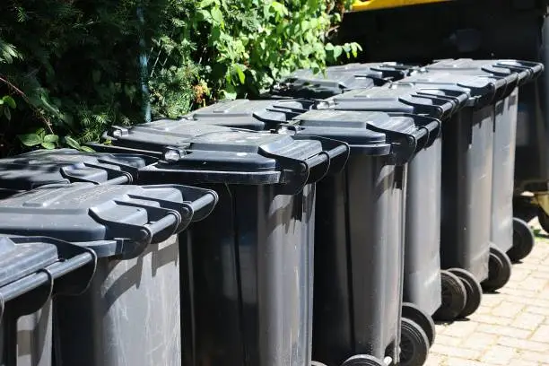 Photo of many black garbage cans are standing in a row