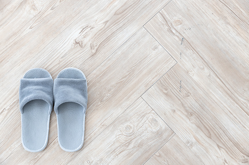 top view of gray pair wool slipper on brown wooden herringbone floor background texture.