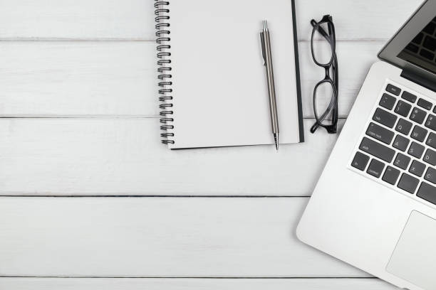 istock Table top view of an empty open notebook with pencil and laptop on white wooden background 1163348399