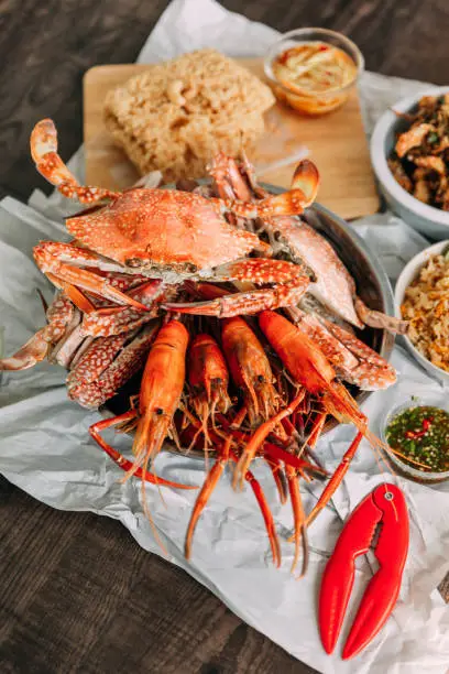 Top view of steamed Flower Crabs and Grilled Prawns (Shrimps) with Crab Cracker on paper with other seafoods in background.