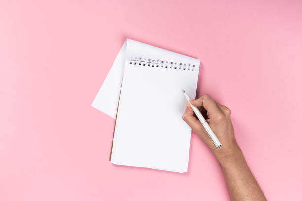 istock Woman's hands with perfect manicure holding pencil and  notepad as mockup for your design. Pink background, flat lay 1163356466