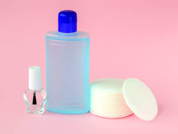 Glass bottle with colorless nail polish, plastic bottle with nail varnish remover and cotton pads on a pastel pink background. Manicure, pedicure, nail care products. stock photo