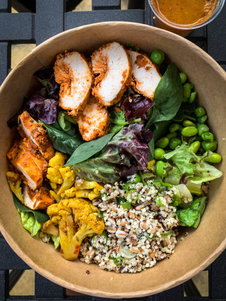 Overhead view of harissa chicken with mixed vegetable, grains, quinoa and harissa dressing on the side in a disposable box