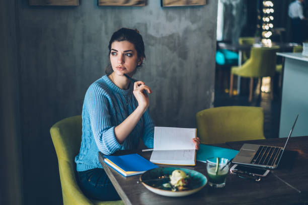 istock Dreamy hipster student sitting at table with laptop computer and thinking on creative ideas for project in modern cafe interior.Thoughtful young woman pondering on plans and looking away 1163365918