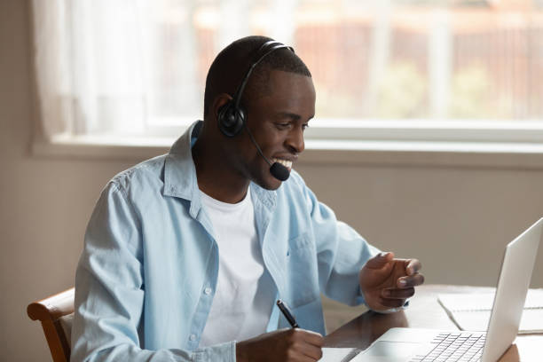 hombre africano usar auriculares haciendo notas estudiando en línea usando la computadora - ready for text audio fotografías e imágenes de stock