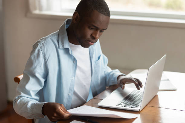 afrikanischer mann sitzt am tisch und bezahlt haushaltsrechnungen mit laptop - human nervous system fotos stock-fotos und bilder