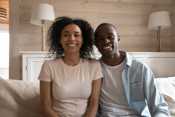 pareja africana sonriente sentada en el sofá haciendo videollamada - relationship difficulties audio fotografías e imágenes de stock