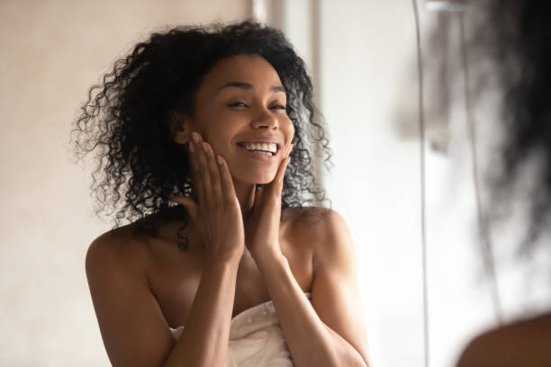 african woman after shower look in mirror touching gentle skin - massage creme imagens e fotografias de stock