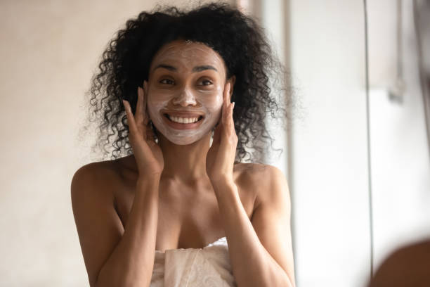 gemischte rasse frau suchen in spiegel anwendung gesichtsmaske - rebellion aging process facial mask beauty treatment stock-fotos und bilder