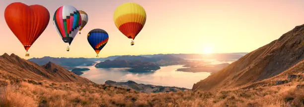 Colorful hot air balloons flying above high mountain at sunrise with beautiful sky background in roys peak track, New Zealand. Panorama of mountain with hot air balloons on morning