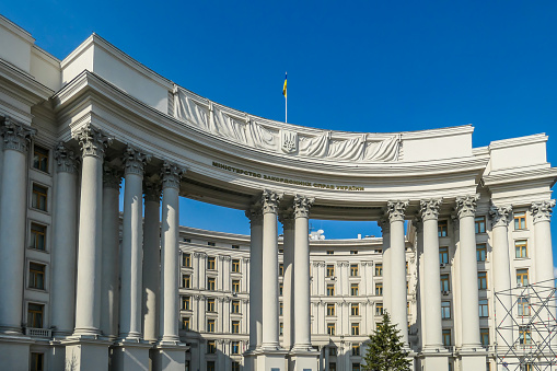 A building of Ministry of foreign Affairs of Ukraine. Marble white arch, with Ukrainian flag on top of it. Arch is supported on thin pillars. Clear and blue sky above the construction