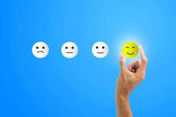 Photo of Conceptual the customer responded to the survey. The client using hand choose happy face smile icon on blue background.Depicts that customer is very satisfied. Service experience satisfaction concept.