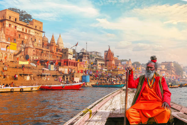 indian sadhu (monk) enjoy boat ride at varanasi ganges river with view of ancient varanasi city architecture and ghat - sadhu imagens e fotografias de stock