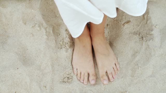 Top view of female bare feet standing on sandy beach