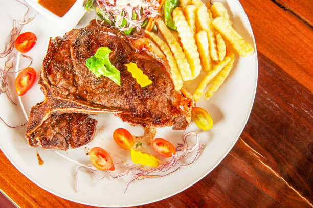 istock Medium rare Grilled T-Bone Steak with salad on white plate on wooden table. 1163376515