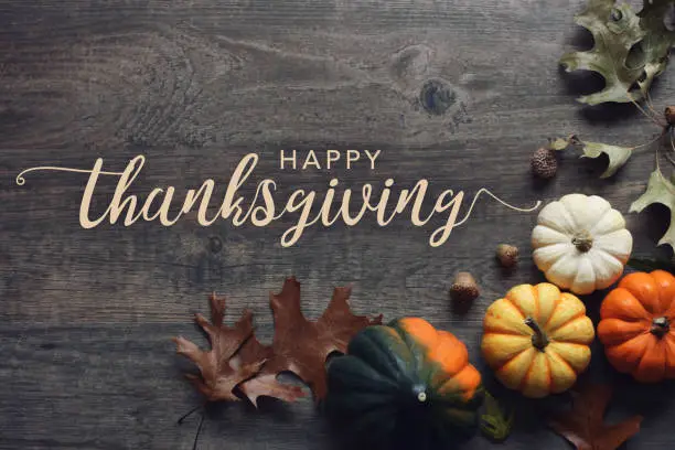 Happy Thanksgiving greeting text with fall pumpkins, squash and leaves over dark wood table background