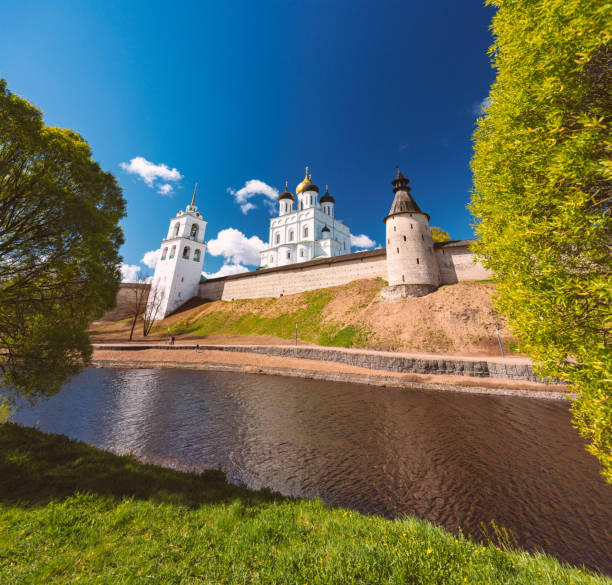 Pskov church and kremlin with blue cloudy sky in background. River in foreground.