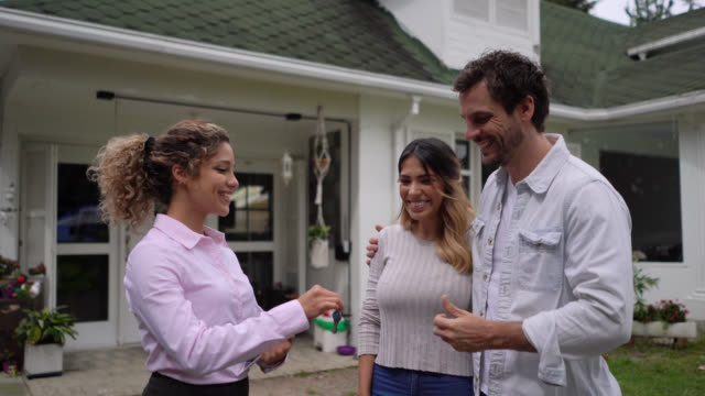 Happy couple closing a deal with female Real Estate Agent at a property smiling while receiving the keys