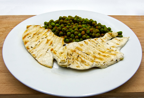 Grilled chicken breasts with peas in tomatoes sauce, studio shot