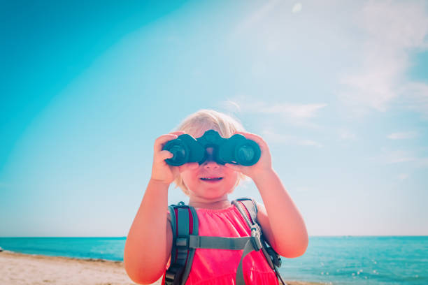 istock little girl with backpack travel on beach, kid looking through binoculars 1163392626