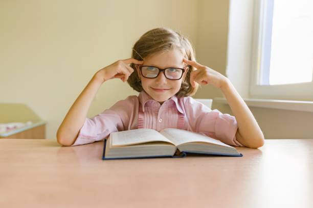 istock Little smart girl with glasses reading large book 1163399728