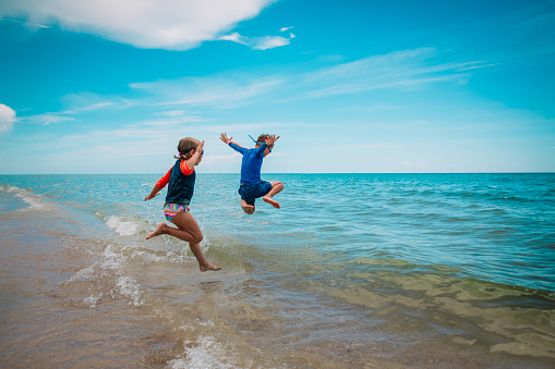 happy kids- girl and boy- run and play with waves on beach