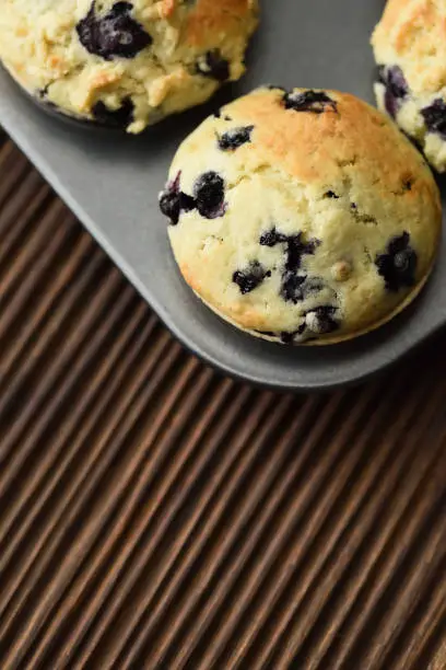 Home baking. Freshly baked blueberry muffins on ribbed oak cutting board top view copy space